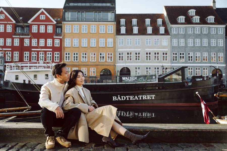 romantic engagement photoshoot in Nyhavn, Copenhagen, capturing a couple sitting by the colorful historic buildings 