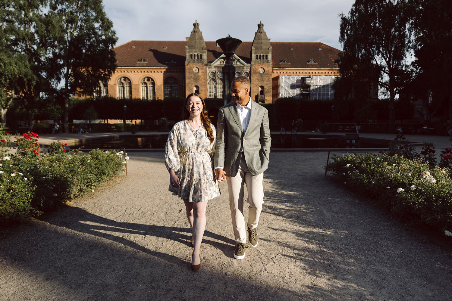 Golden hour engagement photo of a couple walking along a quiet path in the Royal Library Garden